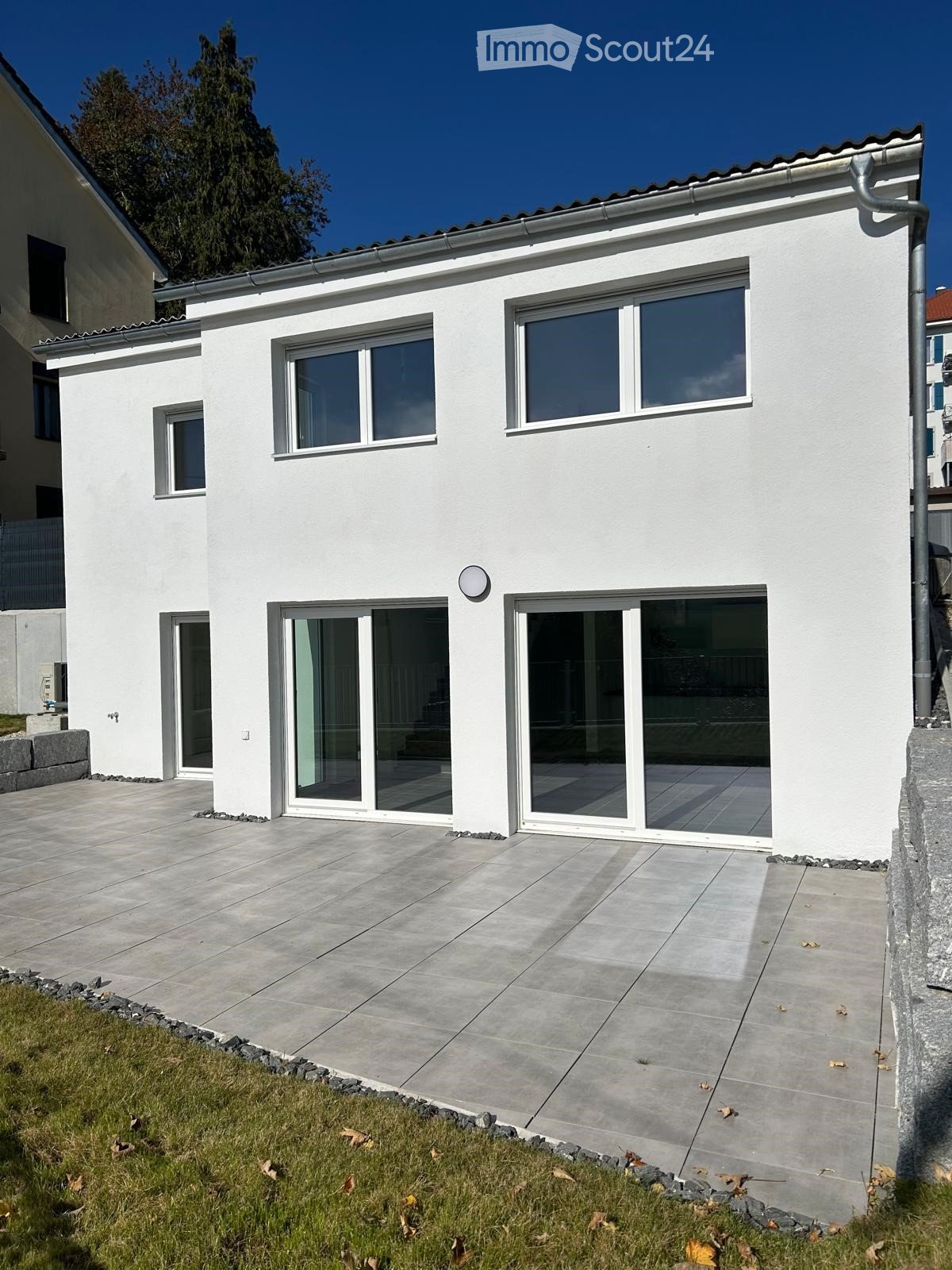 white house, 3 story, double floor, large windows, sliding glass doors, paved front patio