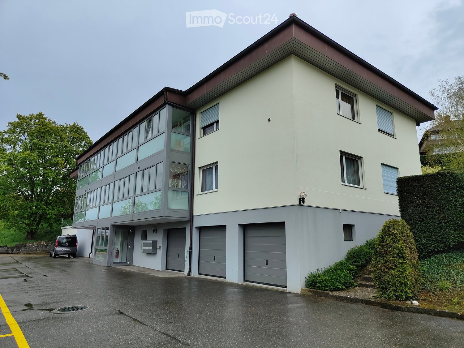 Two story residential building, white exterior, multiple windows, three garages, entrance doors, balcony