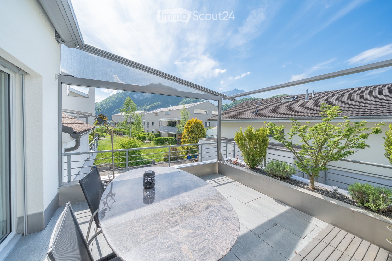Terrace with round table and chairs, metal railing, outdoor lighting, and mountain view.