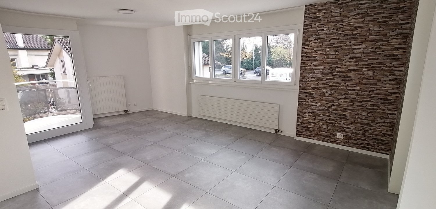white walls, gray tiled floor, glass door to the balcony, two white radiators, brick wall, white sliding window with large glass panes