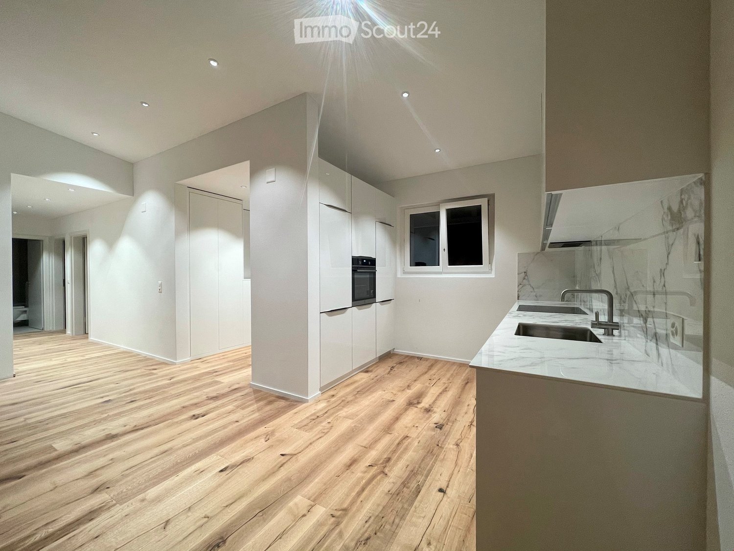 modern kitchen with wooden floor, marble countertops, under-cabinet lighting, double sink, white cabinetry, built-in oven and microwave