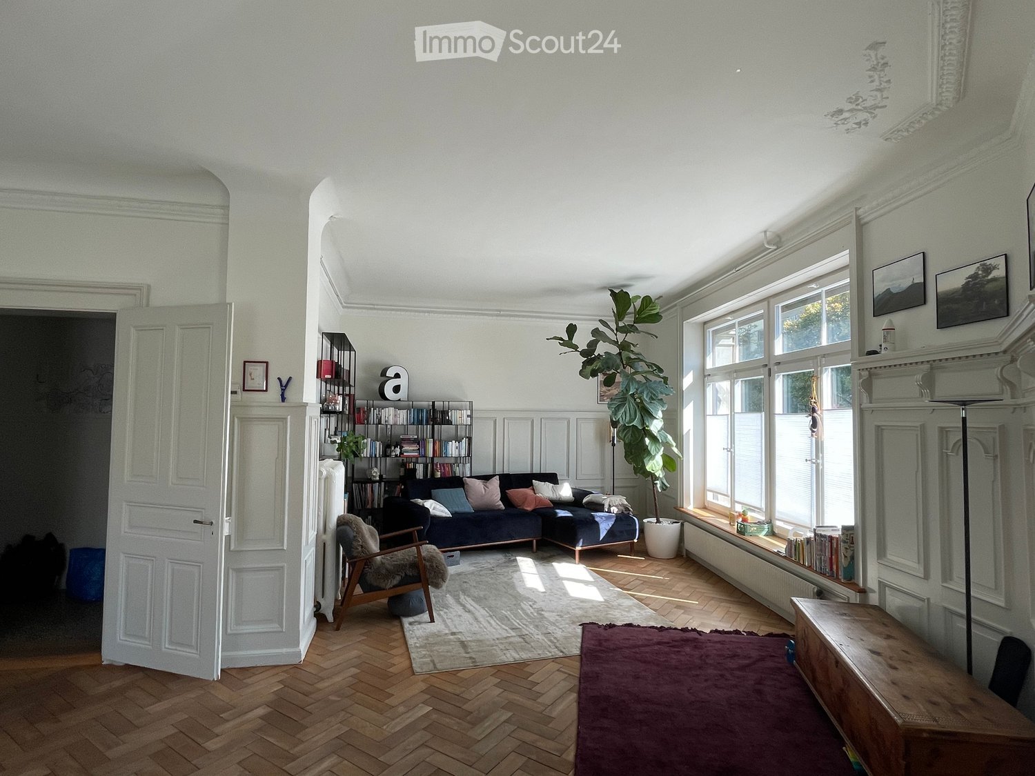 wooden floors, white walls, large windows, white sofa, bookcase, armchair, white rug, tall potted plant, picture frames, window seat