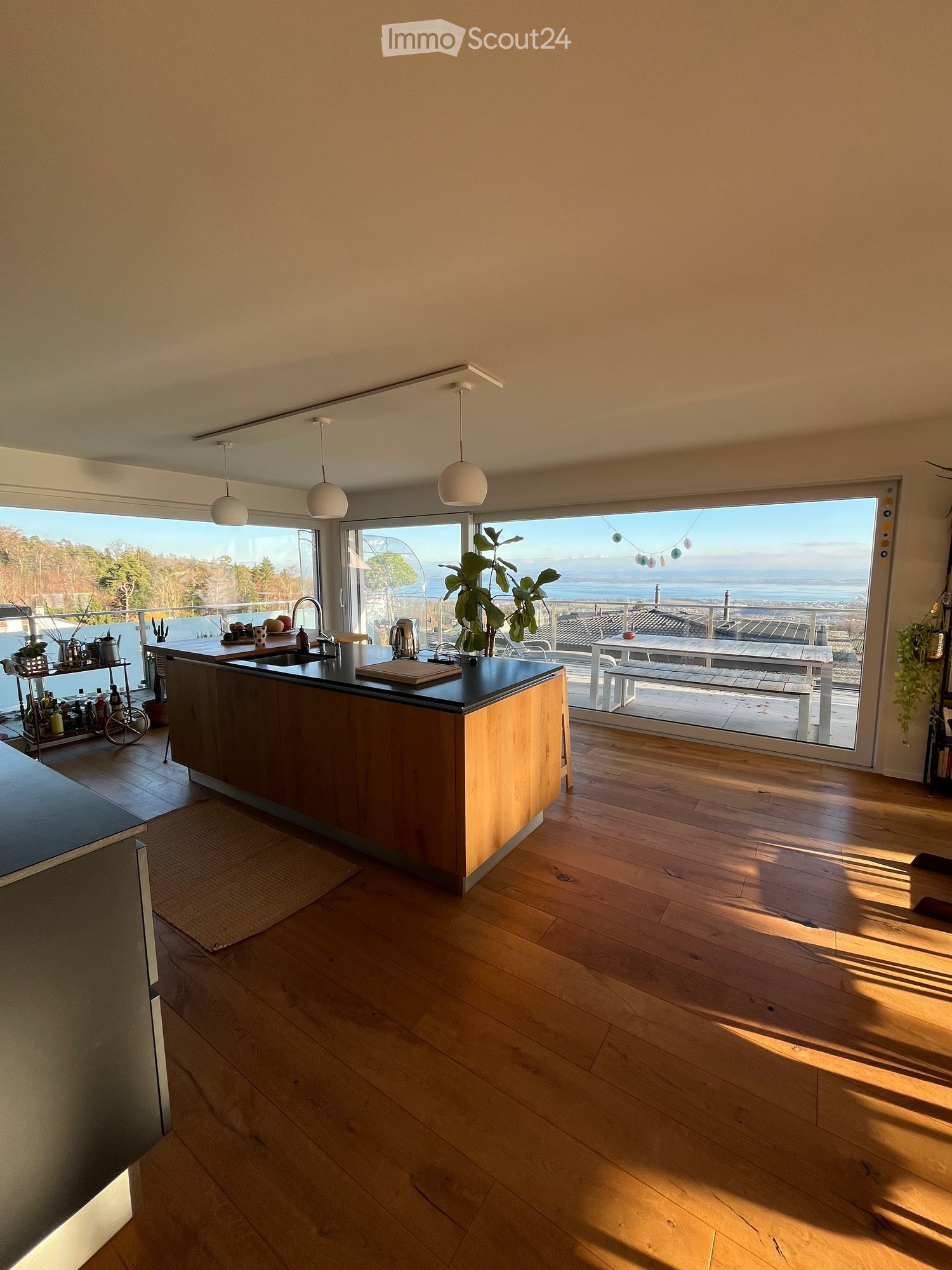 modern kitchen, large wooden island, hanging lamps, large windows, balcony, ocean view