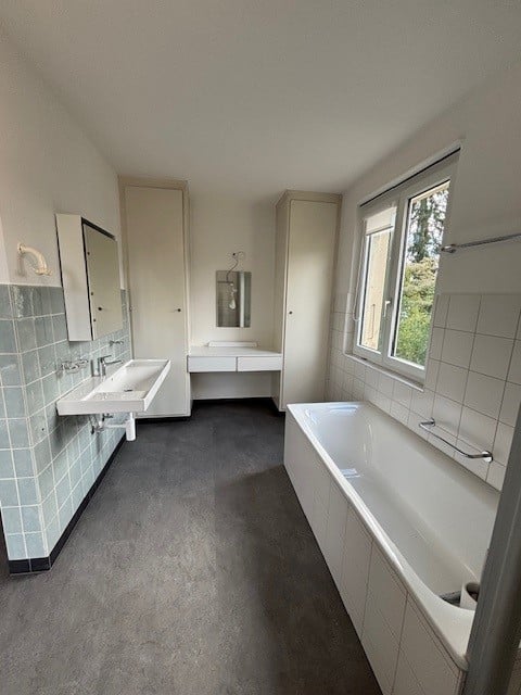 Bathroom with bathtub, sink, mirror, cabinets, blue tiles, white fixtures, window