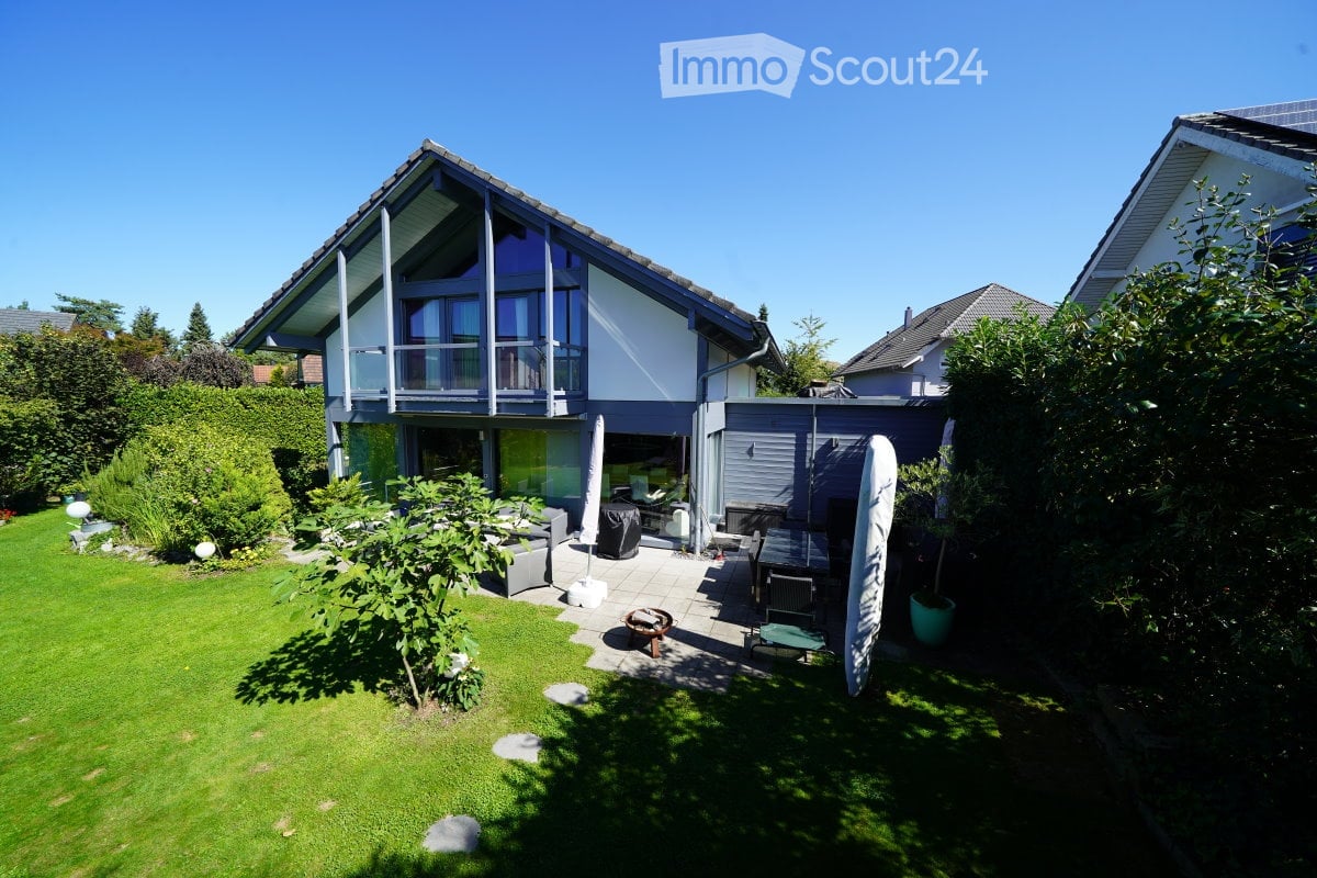 Detached house with glass balcony, garden with outdoor seating, greenery, solar panels on adjacent house