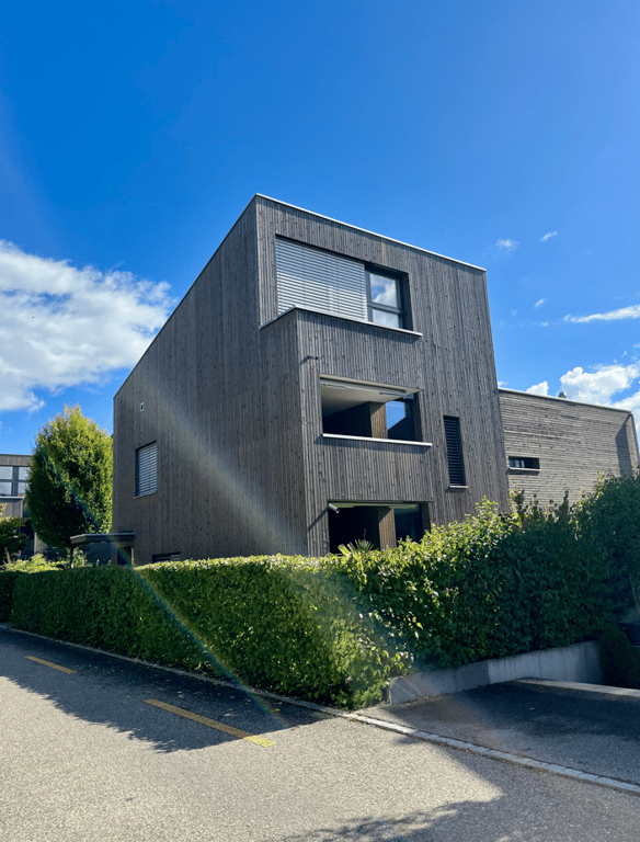 3-story modern building, dark grey wooden facade, multiple windows, elevated ground floor