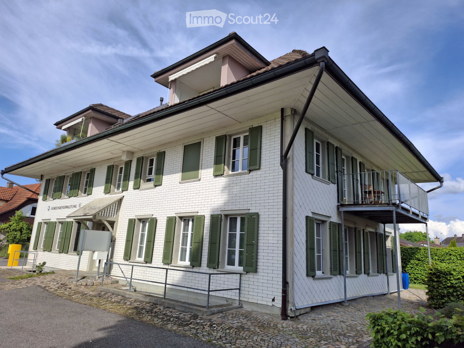 White brick house, green shutters, multiple windows, balcony on the second floor, small pathway leading to the entrance