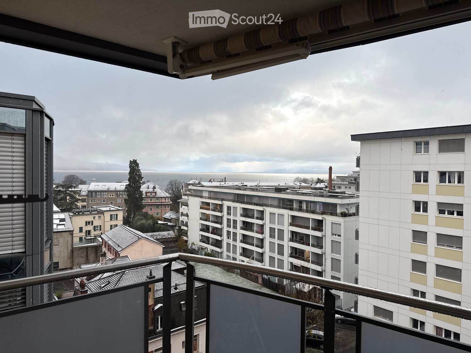 Balcony overlooking cityscape with mountains in the distance, large windows, metal railings, cloudy sky