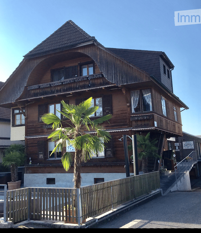 large wooden house, two storeys, three balconies, two potted trees