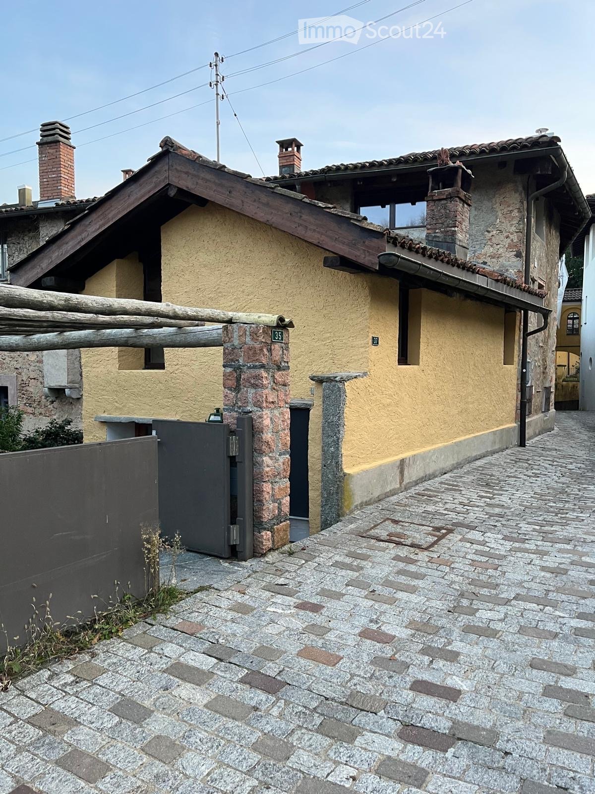 2 story house, yellow exterior, brick chimneys, gated entrance, cobblestone driveway