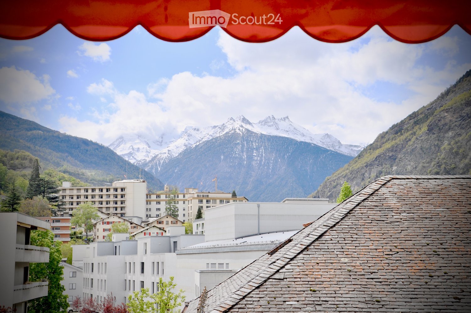 rooftop view, multiple buildings, snowy mountains in background, cloudy sky