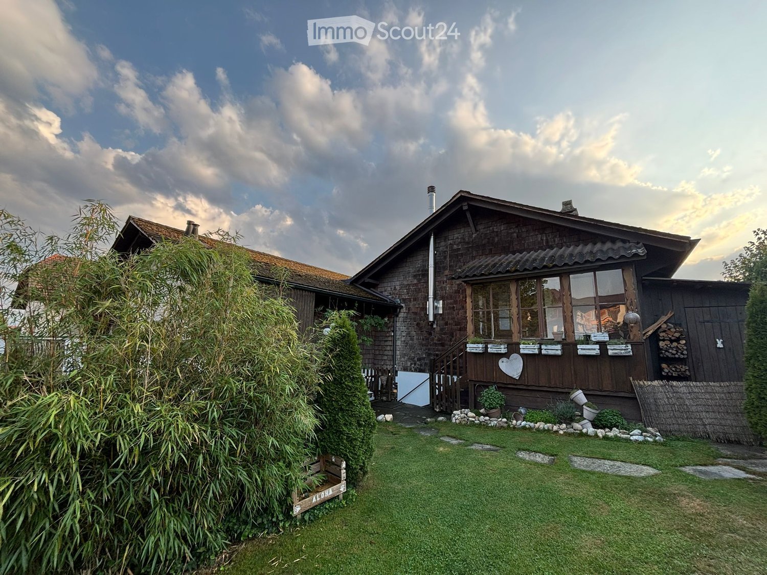 Wooden house, chimney, glass windows, front yard with wooden steps and plants, log pile, wooden fence