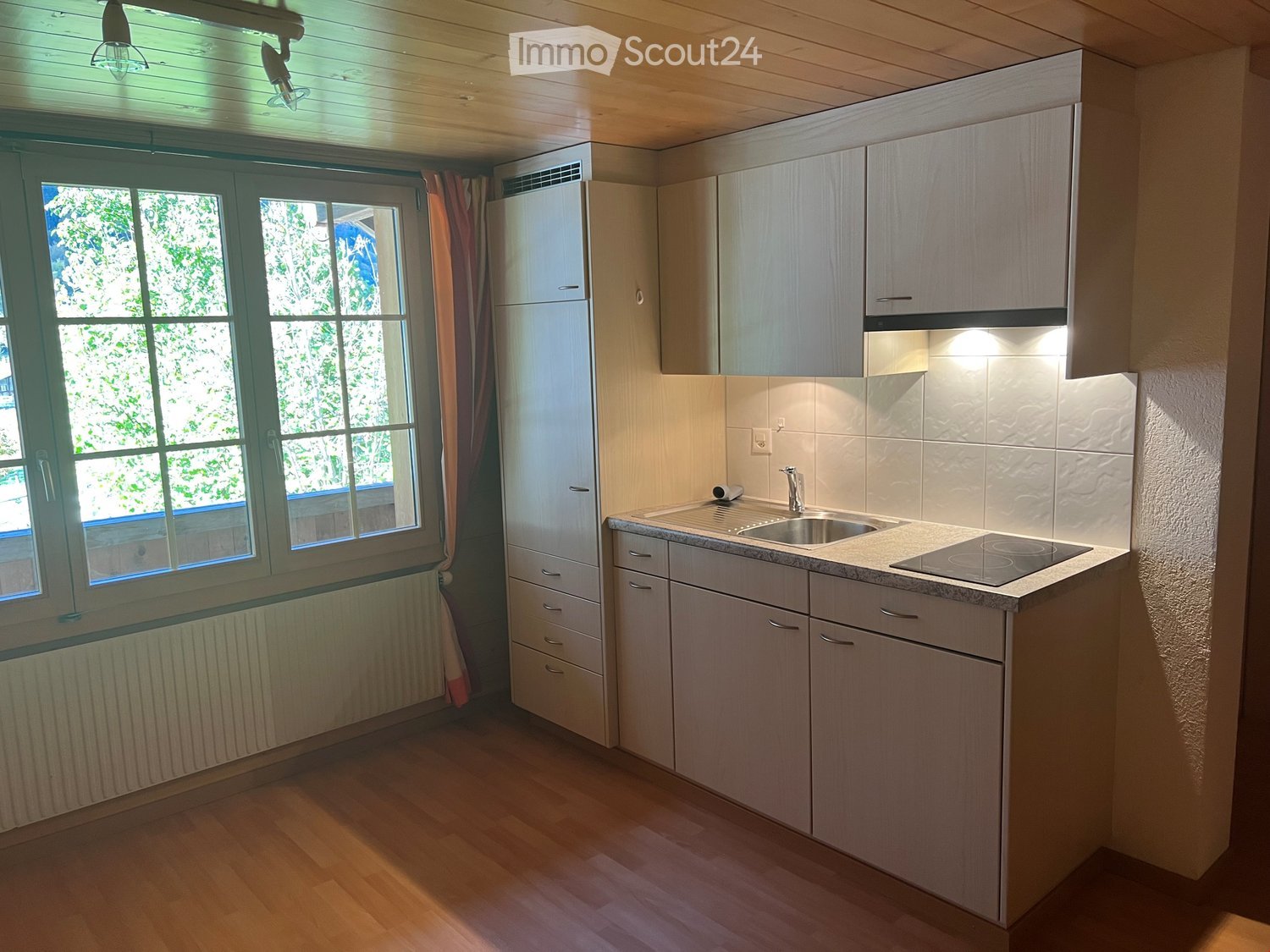 Modern kitchen with wooden flooring, white cabinetry, stainless steel sink, gas stove, windows, and wall-mounted heater.