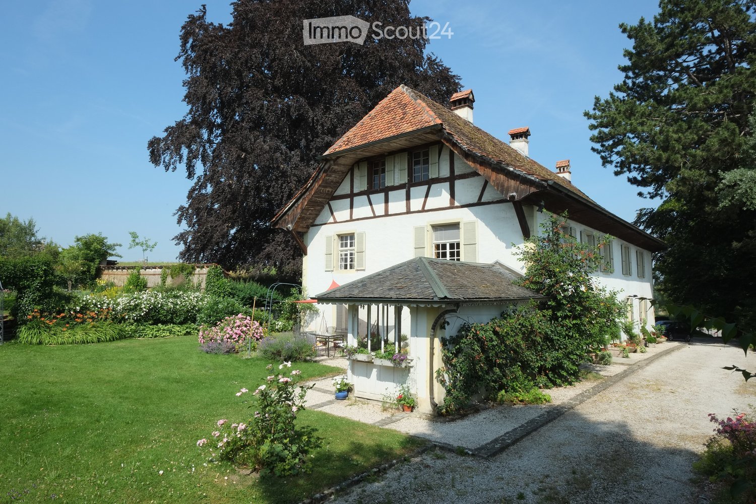 2-story house, white exterior, brown roof, several windows, attached carport, garden, various plants, well-manicured lawn