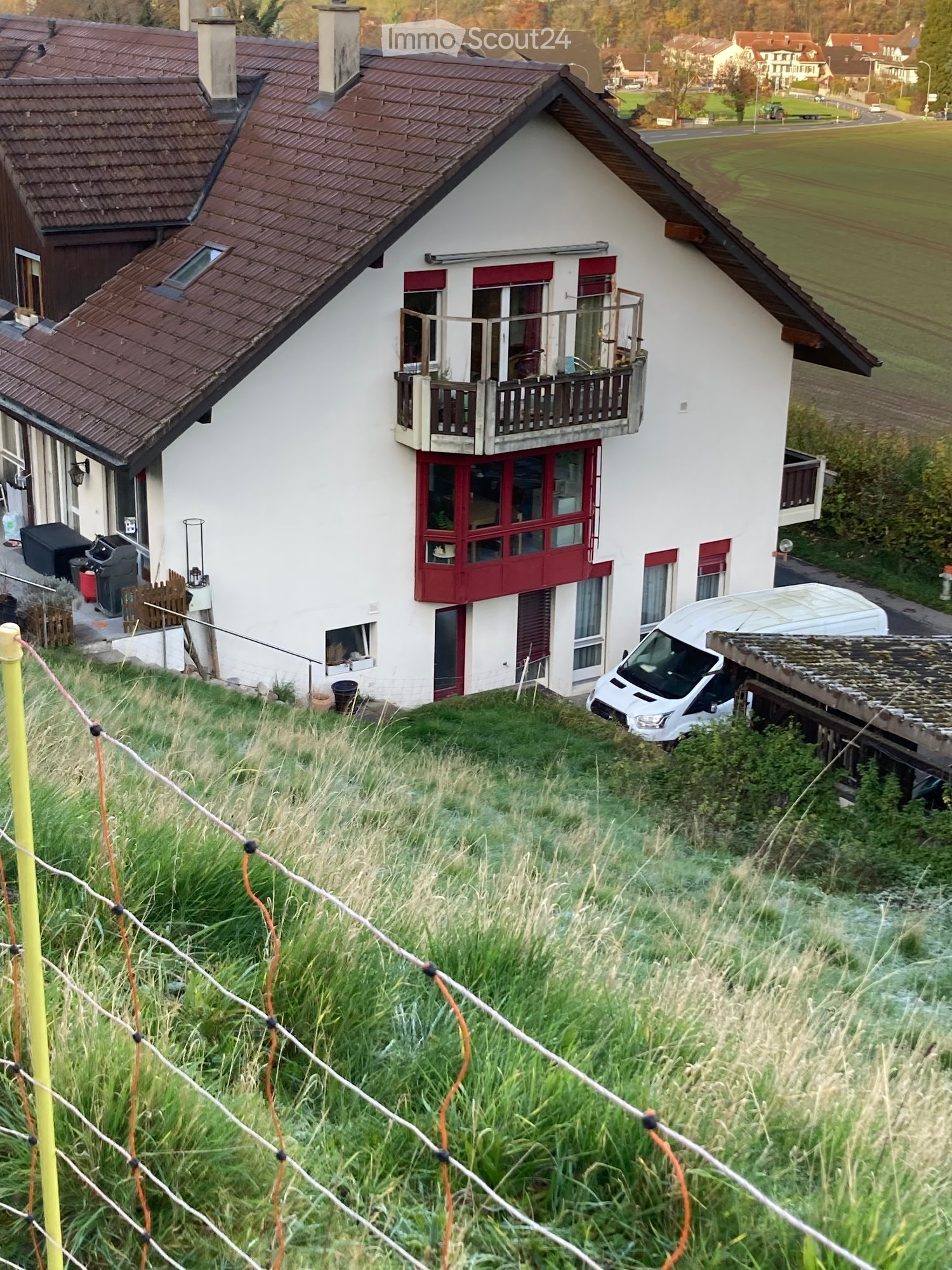 detached house with brown roof, balcony, chimneys, glass windows, white walls, red window frames, fenced area
