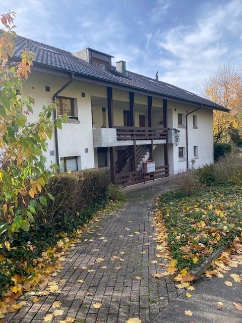 two-story white house, wooden balconies, brick walkway, bushes and fallen leaves