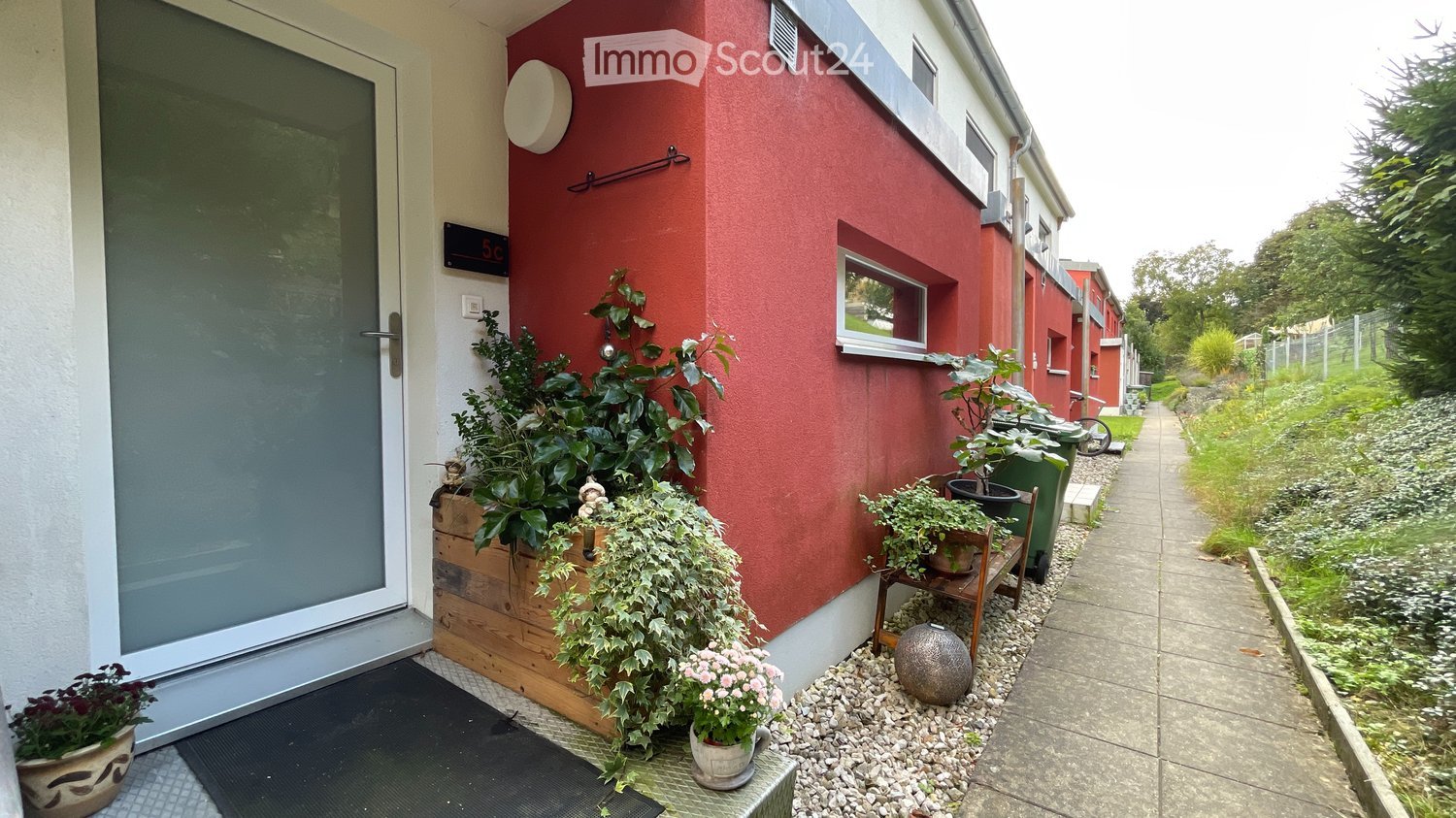 A residential building with a red exterior wall and a white-framed glass door, accompanied by potted plants outside.