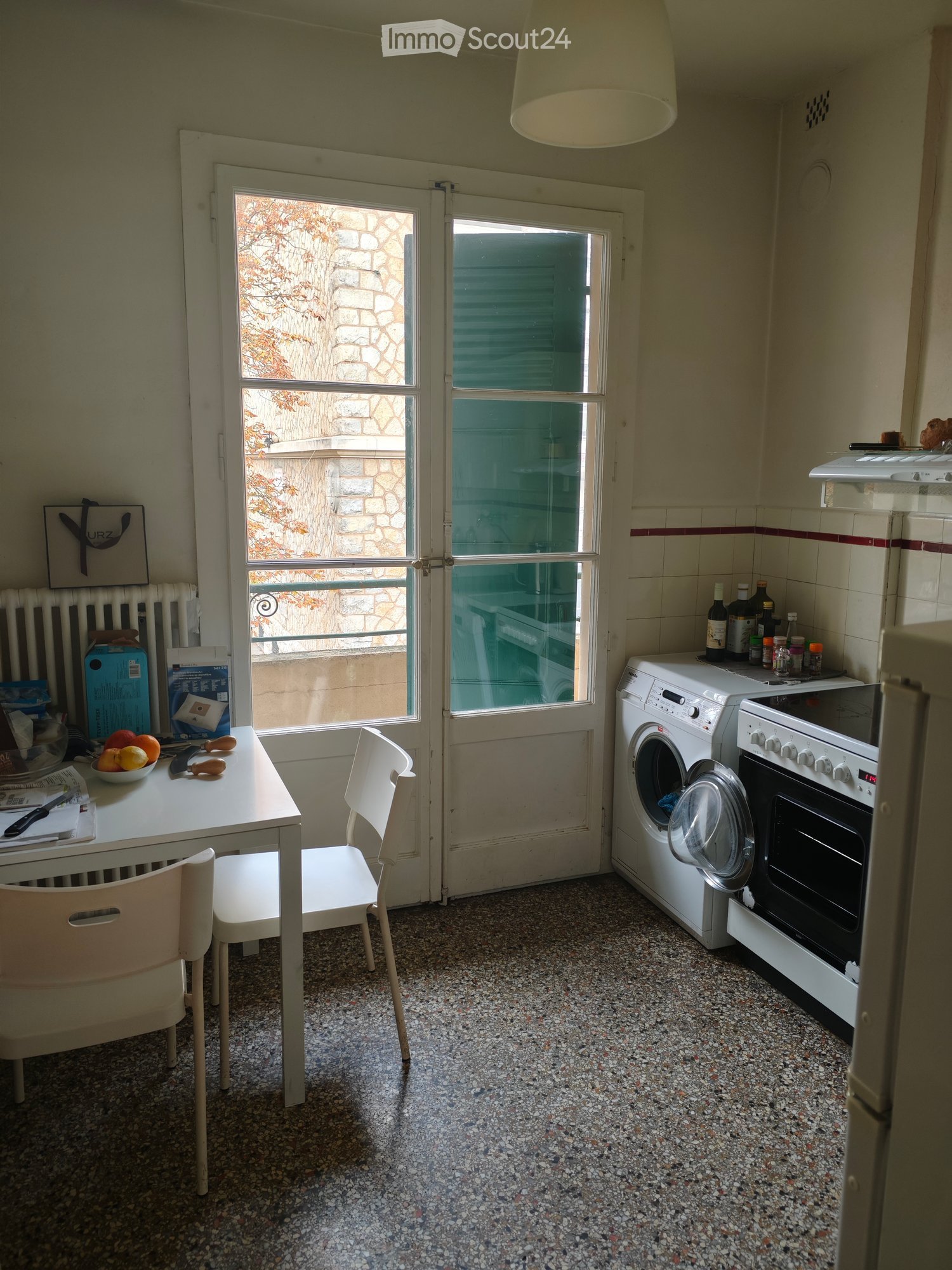 The kitchen is a small area, with a washing machine, stove, and a table with chairs. A door leads to the outside.