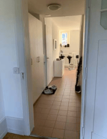 empty corridor, white walls, beige tiles, light switches, small table with items, black shoes on rug