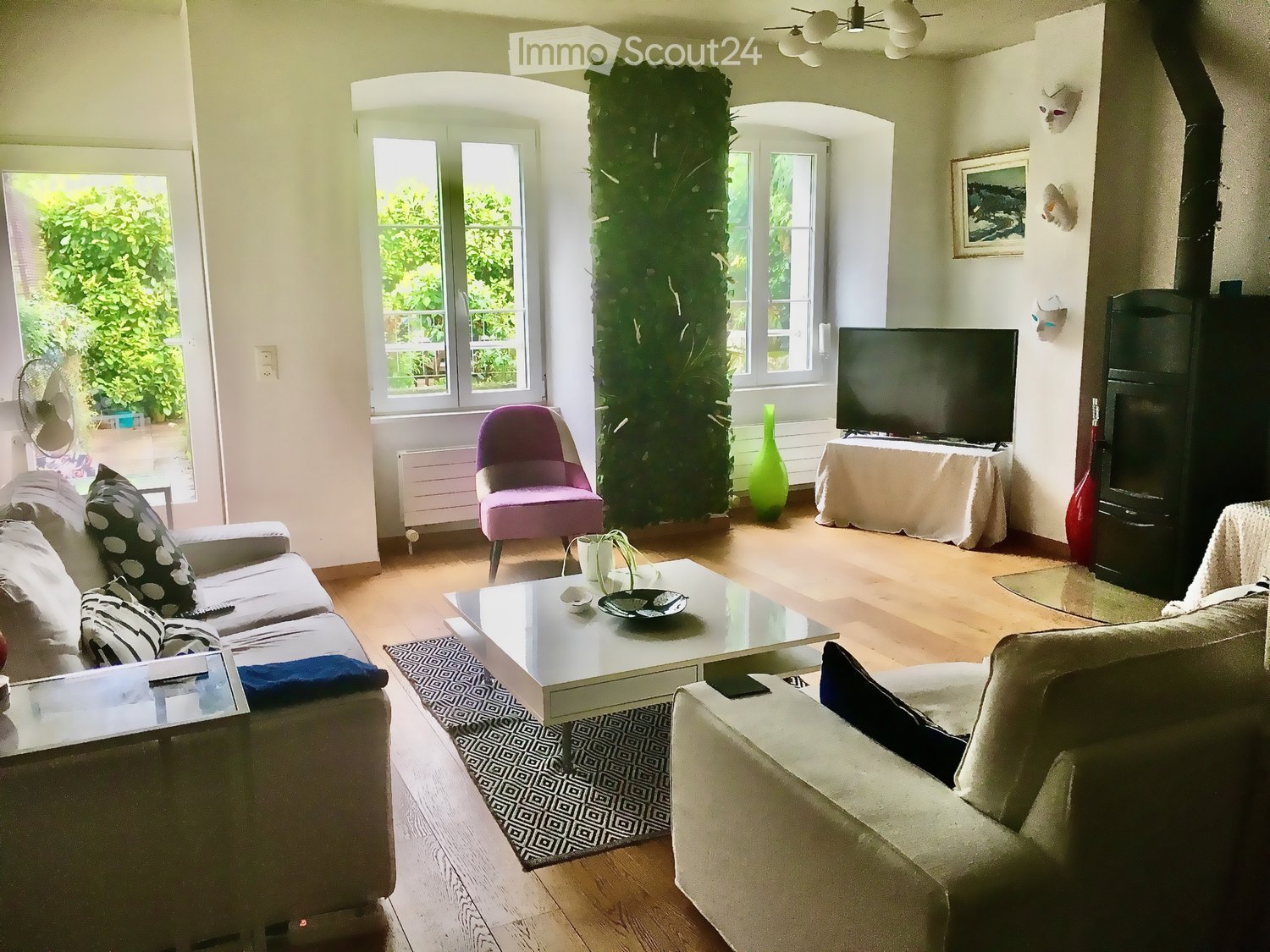 Living room with couches, coffee table, armchair, television, potted plant, radiator, wooden floor, fireplace, picture frame, windows