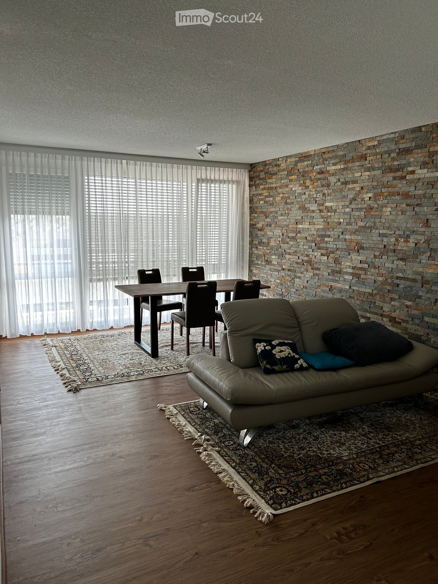 large living room, dining area, stone wall, carpet, couch, dining table, windows with blinds