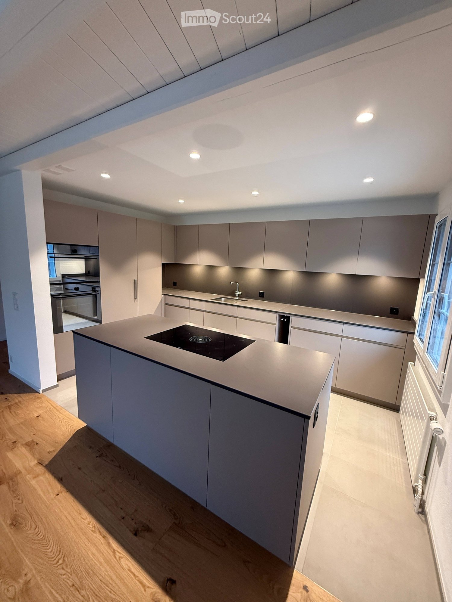 Modern kitchen with island, built-in oven, sink, large window, central heating