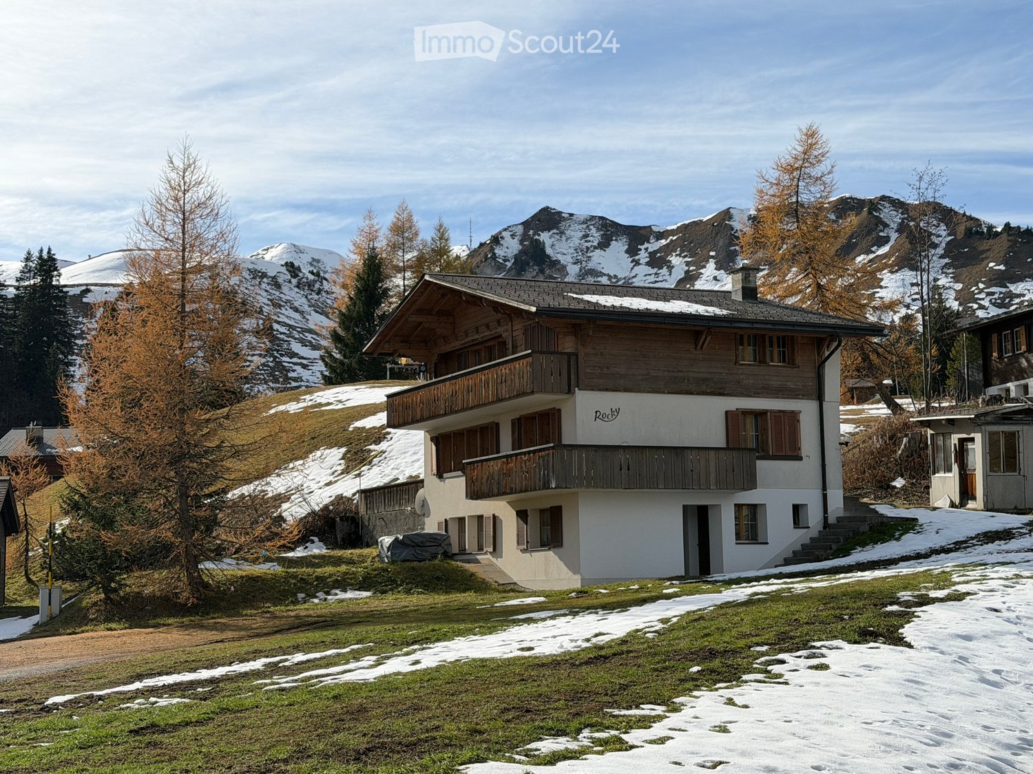 2 story building, wooden balconies, located on a slope, snow on ground, mountain view