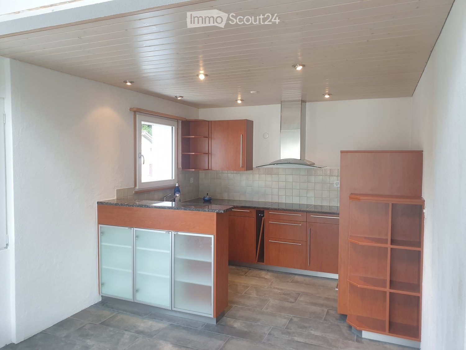Modern kitchen with wooden cabinets, granite countertops, sink, tiled backsplash, overhead lighting, dishwasher, and an open window.