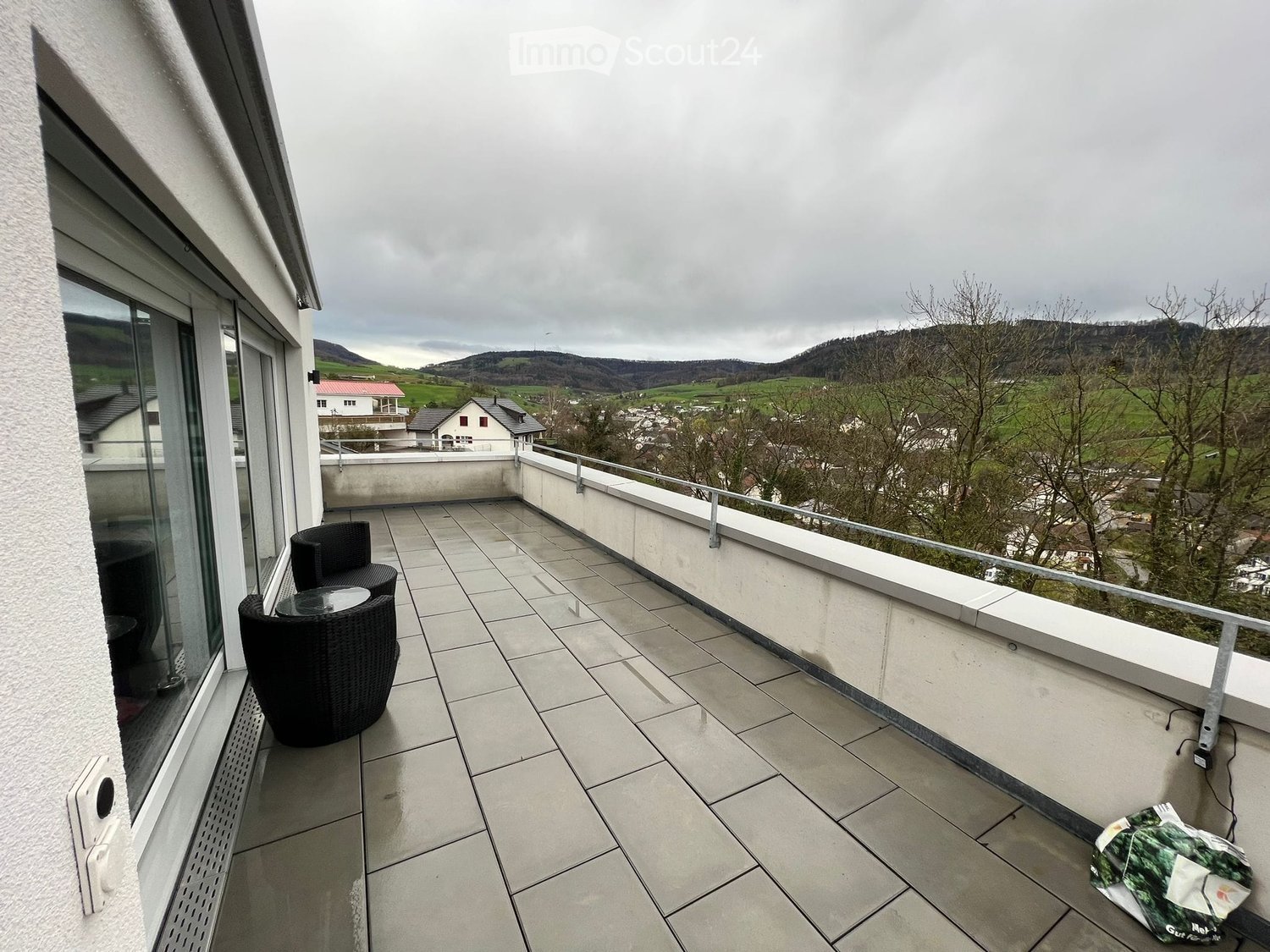 terrace with tile flooring, two black round tables, metal railing, view of mountains and village