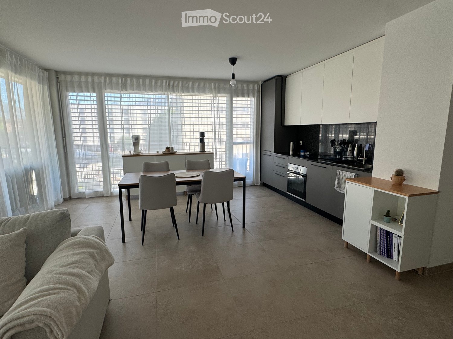 Dining area with table and chairs, modern kitchen with appliances, beige couch