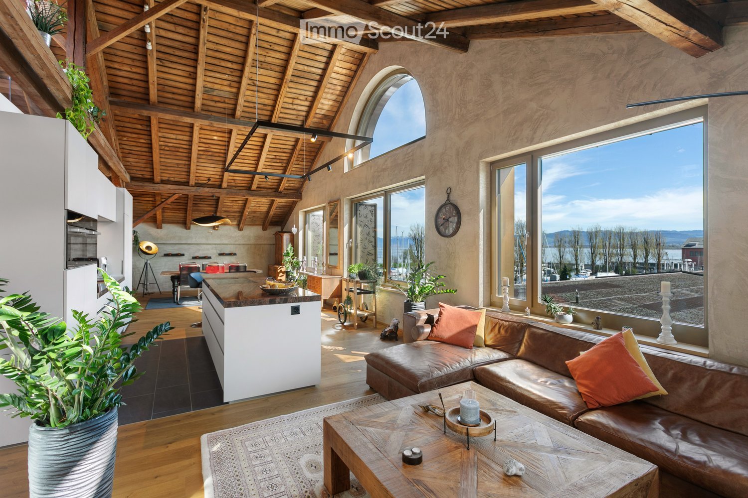 Living room with wooden ceiling, wooden floor, large windows, brown sofa, wooden table, plants