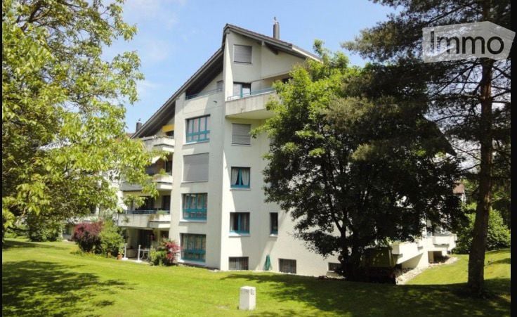 white building, 3 floors, multiple windows, balconies, surrounded by trees and grass