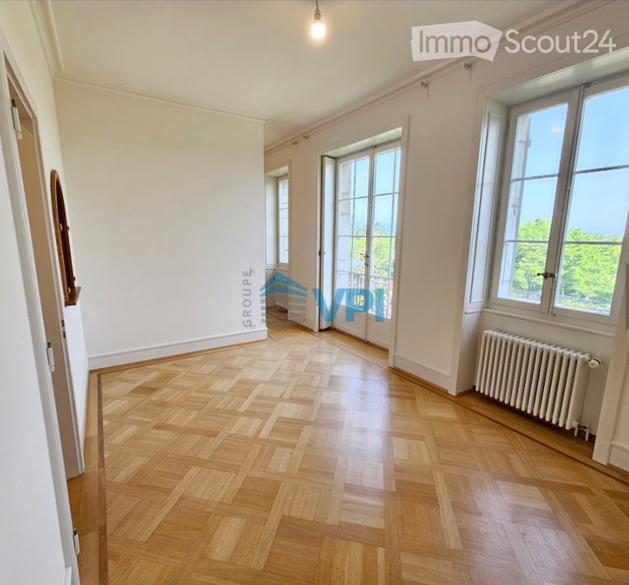 A hallway with parquet floors, white walls, two doors, large windows, and a radiator