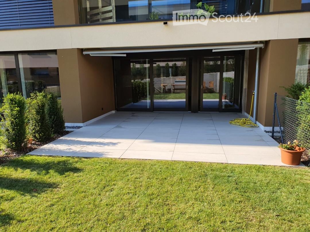 tiled flooring, glass doors, plants, bench, chain link fence, outdoor plants, shrubs, green grass, paved area