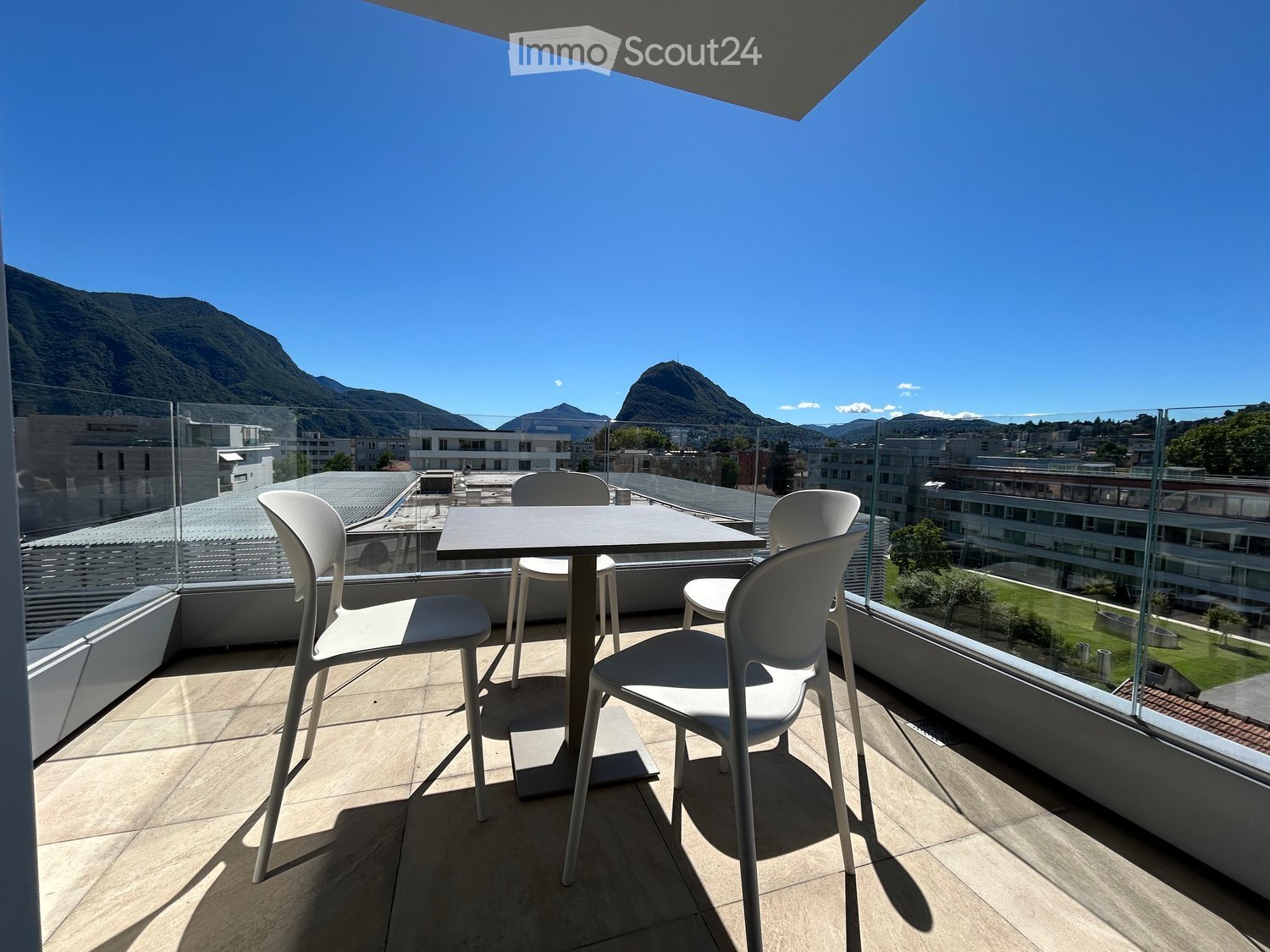Balcony with table and chairs, surrounded by glass walls, view of mountains and cityscape