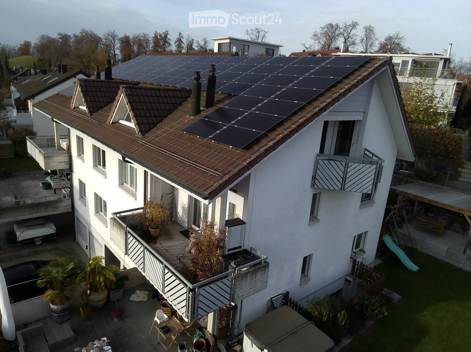 4 story house, brown roof, solar panels, multiple balconies, garden, car parked in driveway