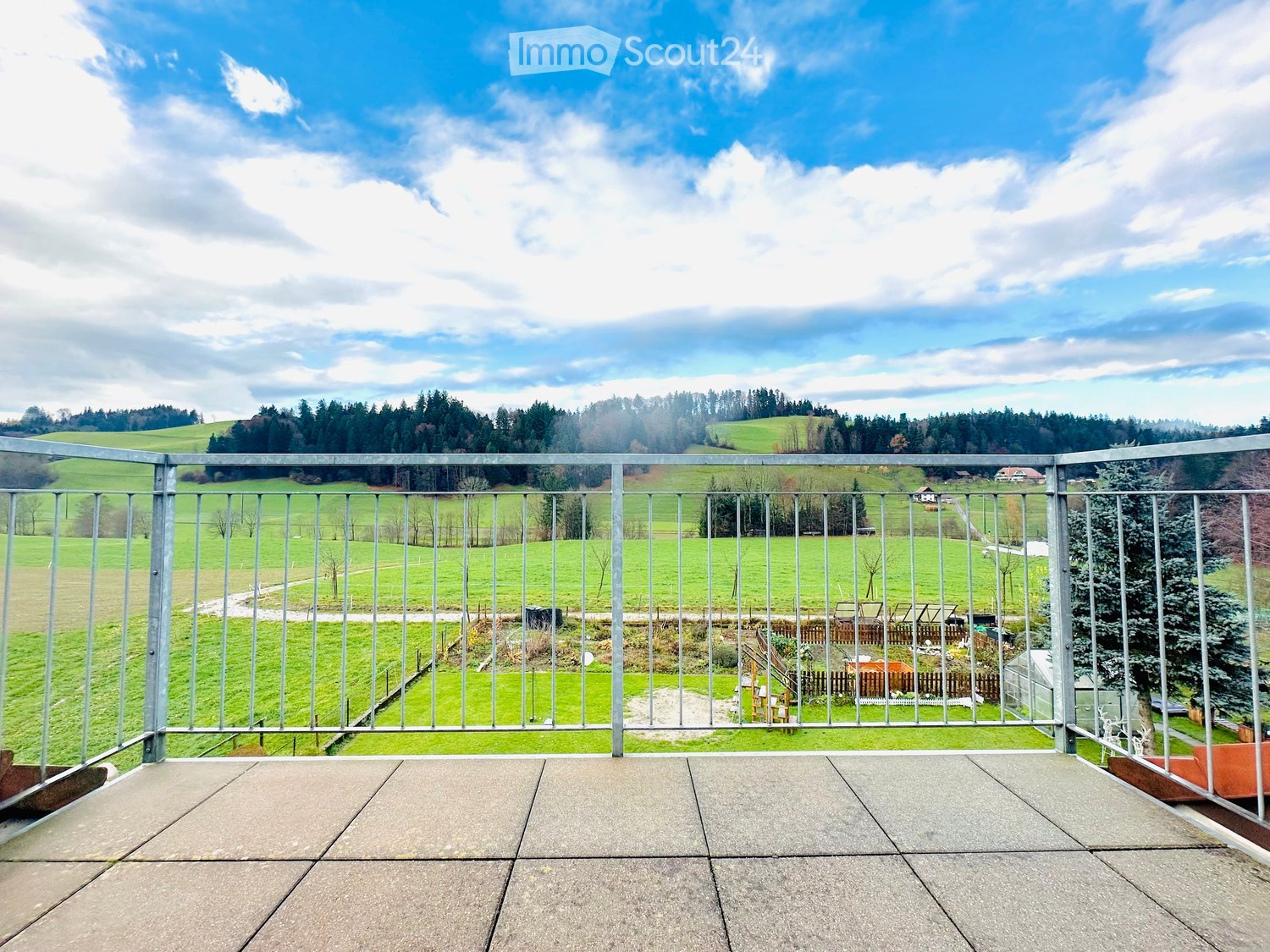 Terrace with green railing, view of a green field with trees
