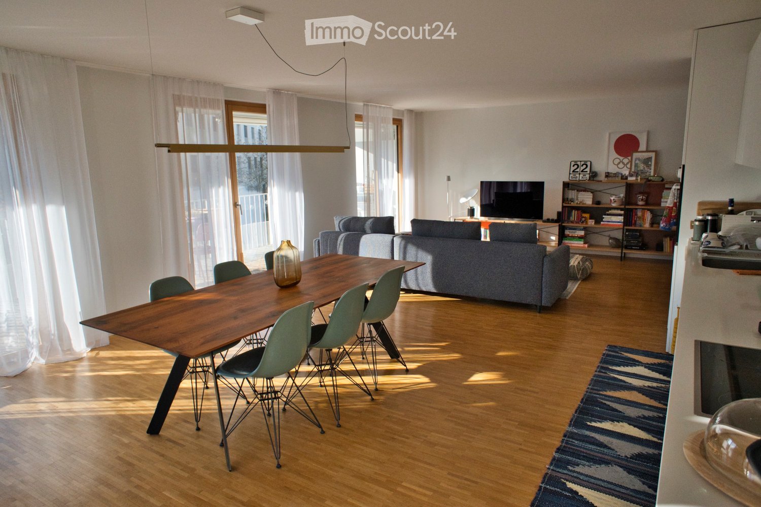 large open room, wood flooring, modern table and chairs, grey couch, television, bookshelf