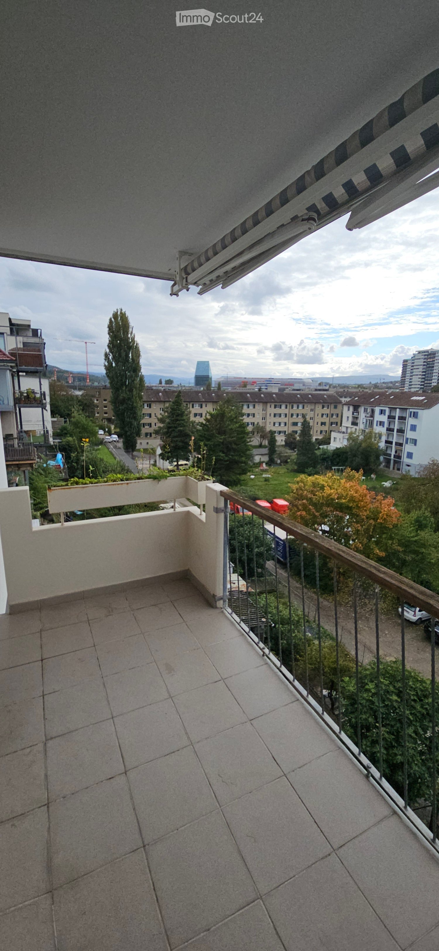large balcony with tiles, metal railing, plant pot, cityscape view