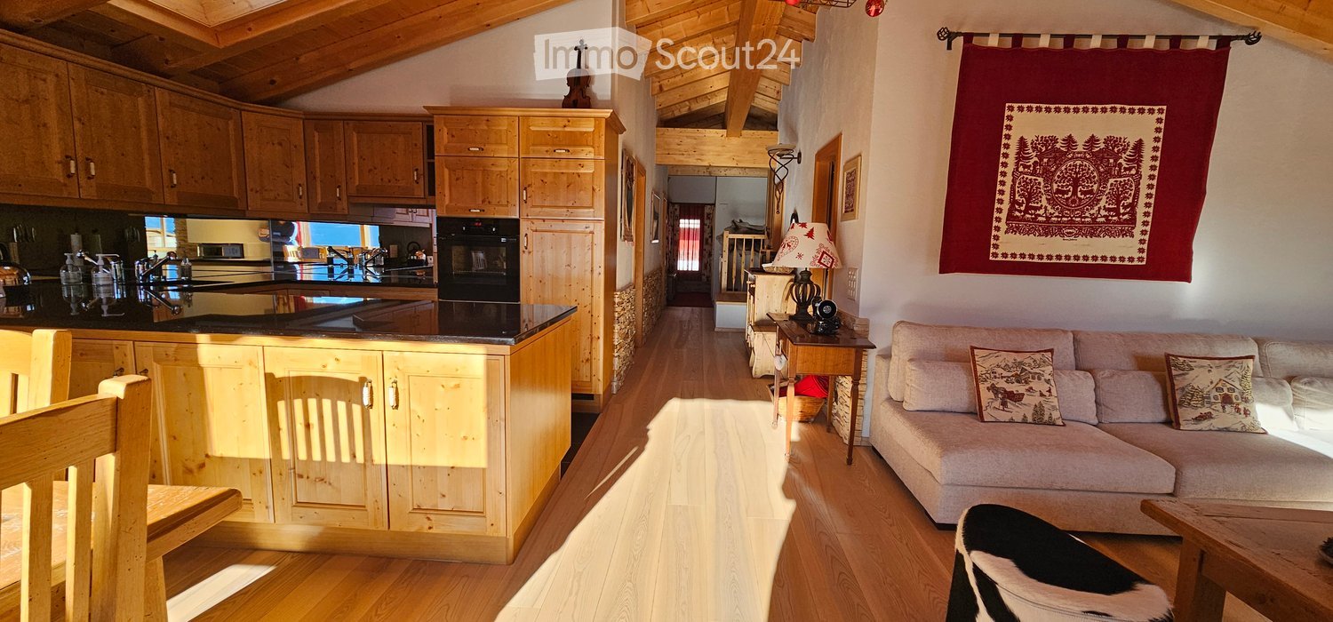 Open plan kitchen and living room with wooden cabinets and flooring, built-in oven, sofa, lamp, tapestry, wooden chair, dining table