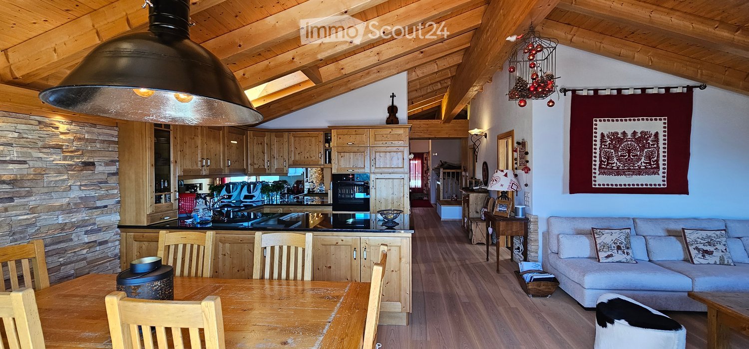 Wooden ceiling, wooden dining table and chairs, wooden cupboards, open kitchen, sofa with cushions, coffee table, pendant lamp, lamp on side table, rug, wooden floor, wooden wall with brick-like texture