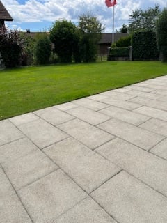 Well-maintained lawn, brick path, distant flag, greenery, clear blue sky