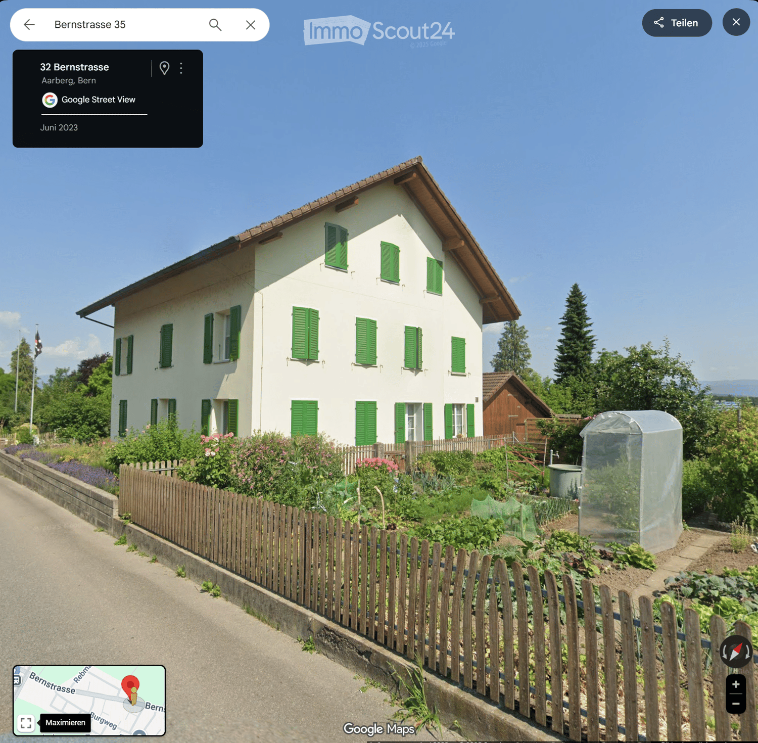 House, white exterior, green shutters, garden in front, visible road and trees in background