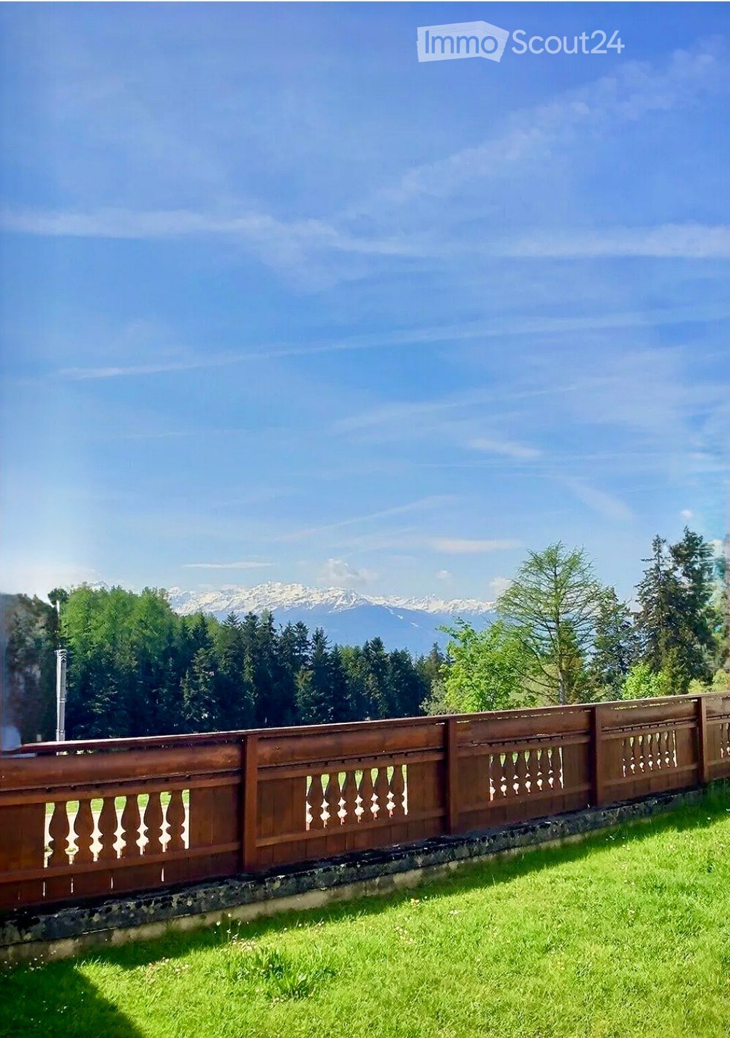 Green grass, brown wooden fence, blue sky, trees, mountains