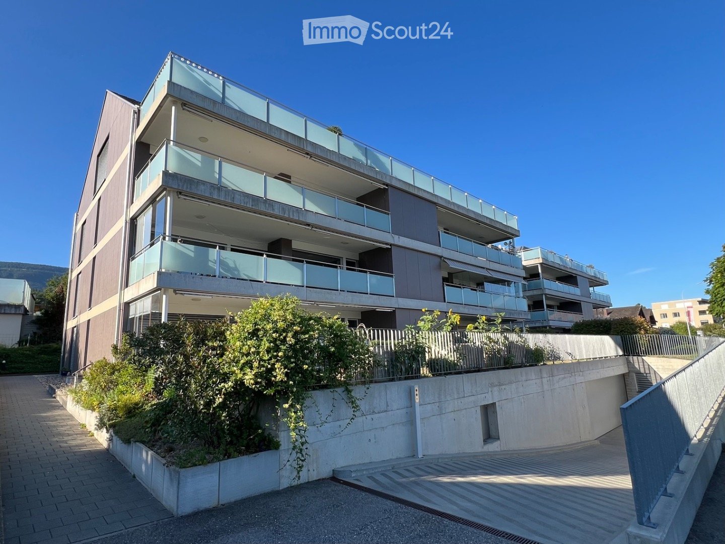 modern multistory building, gray concrete walls, balconies, fenced terrace, pathway, greenery