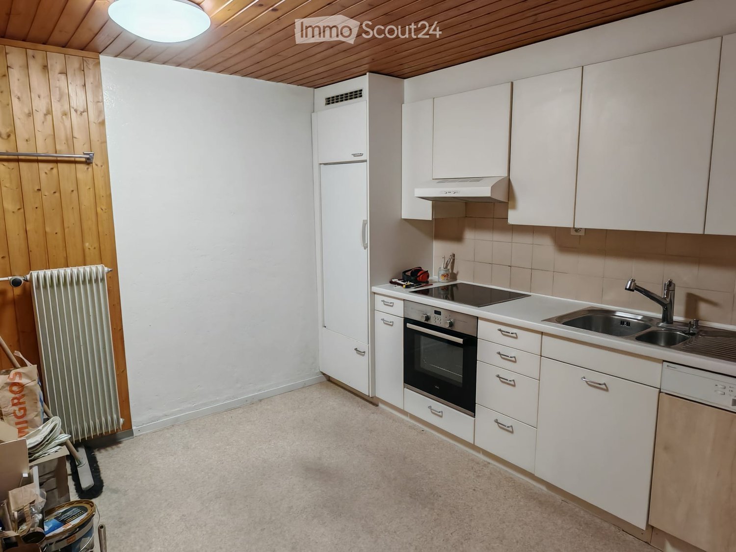Modern white kitchen with white cabinets, tiled walls, white countertop, built-in appliances, and a wooden ceiling.