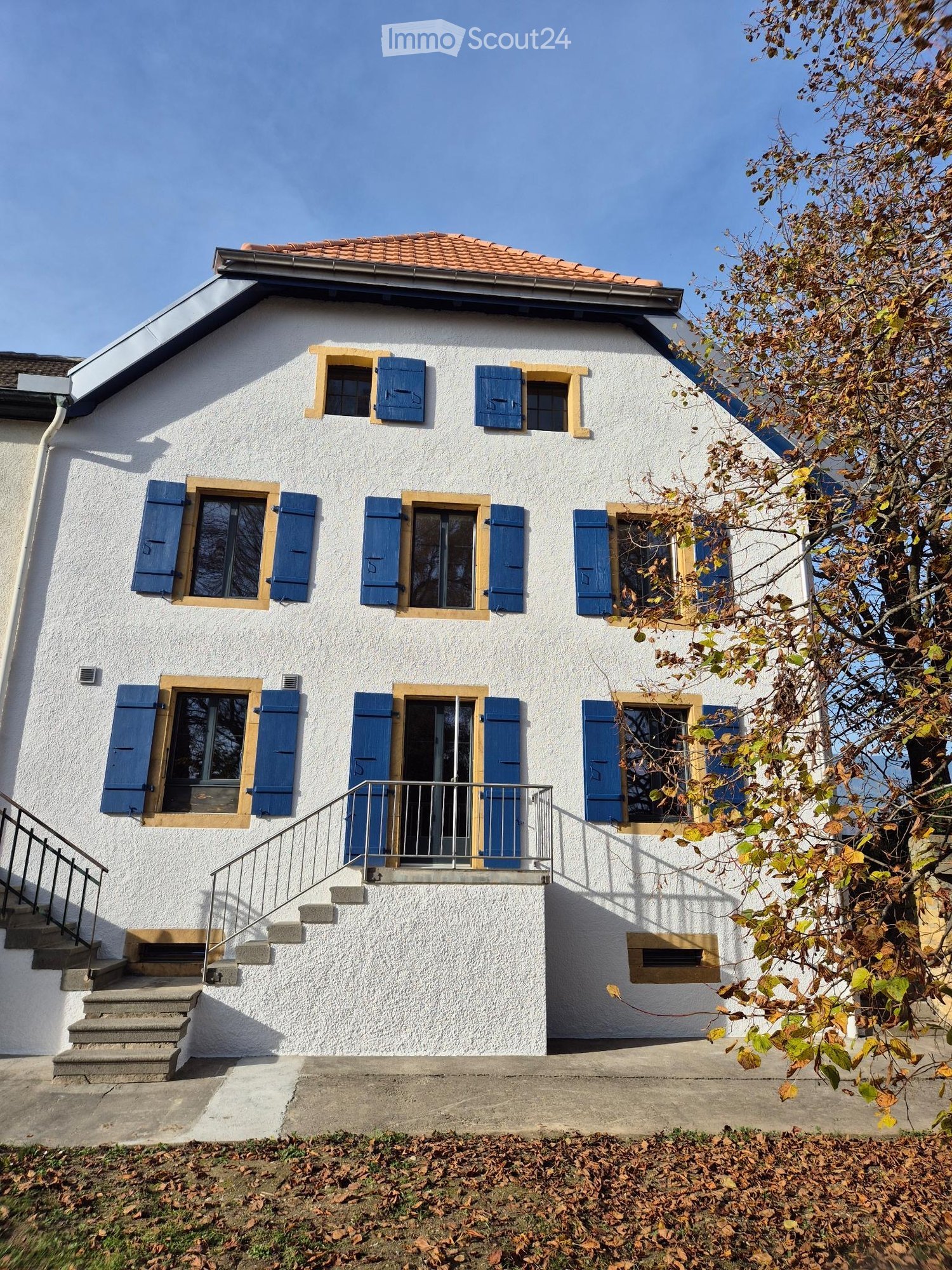 white painted building with blue shutters and a red roof, steps leading to the entrance, clear sky background