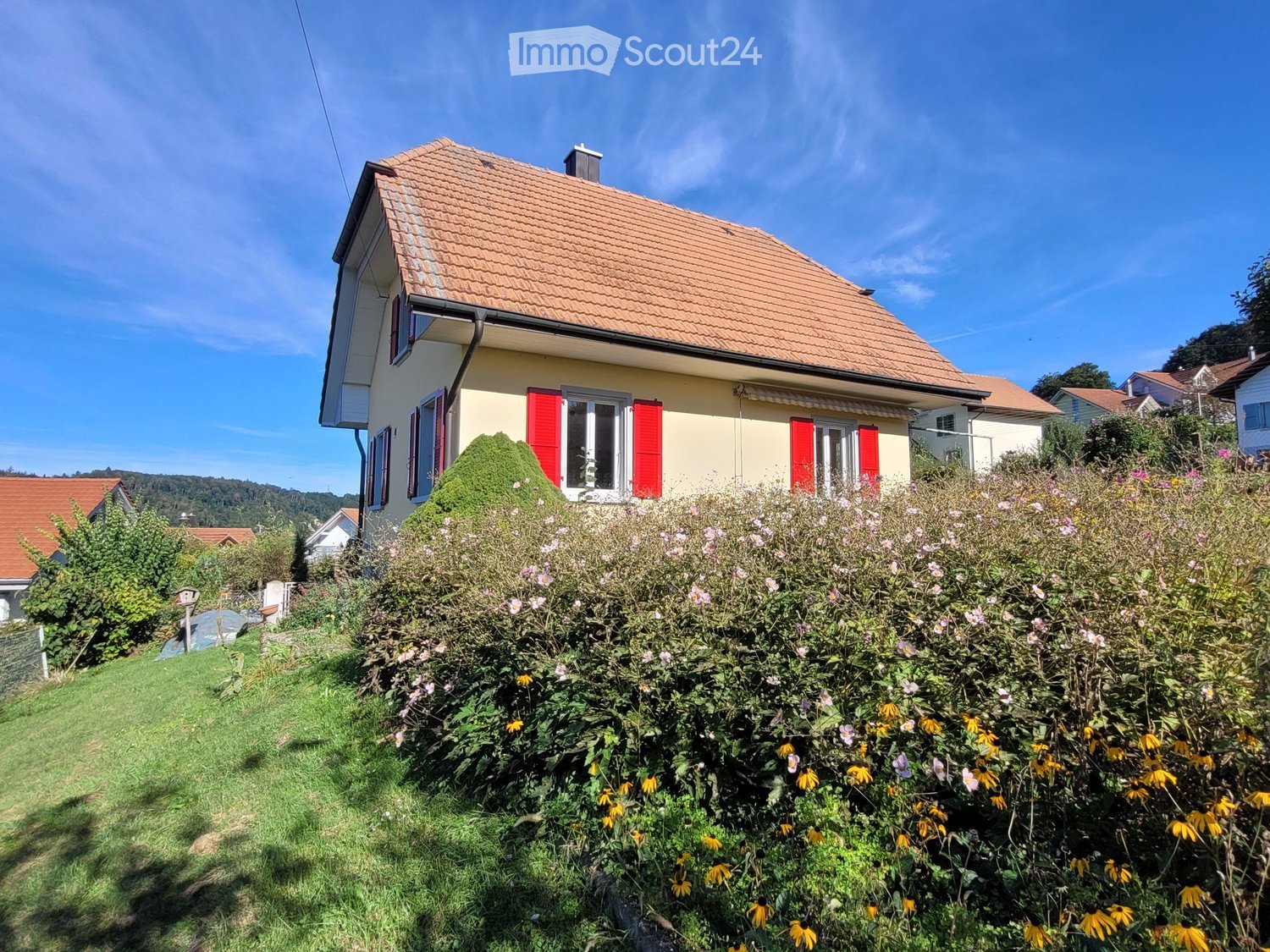 2 story house, yellow exterior, red shutters, brown roof, garden with various flowers, well-kept yard