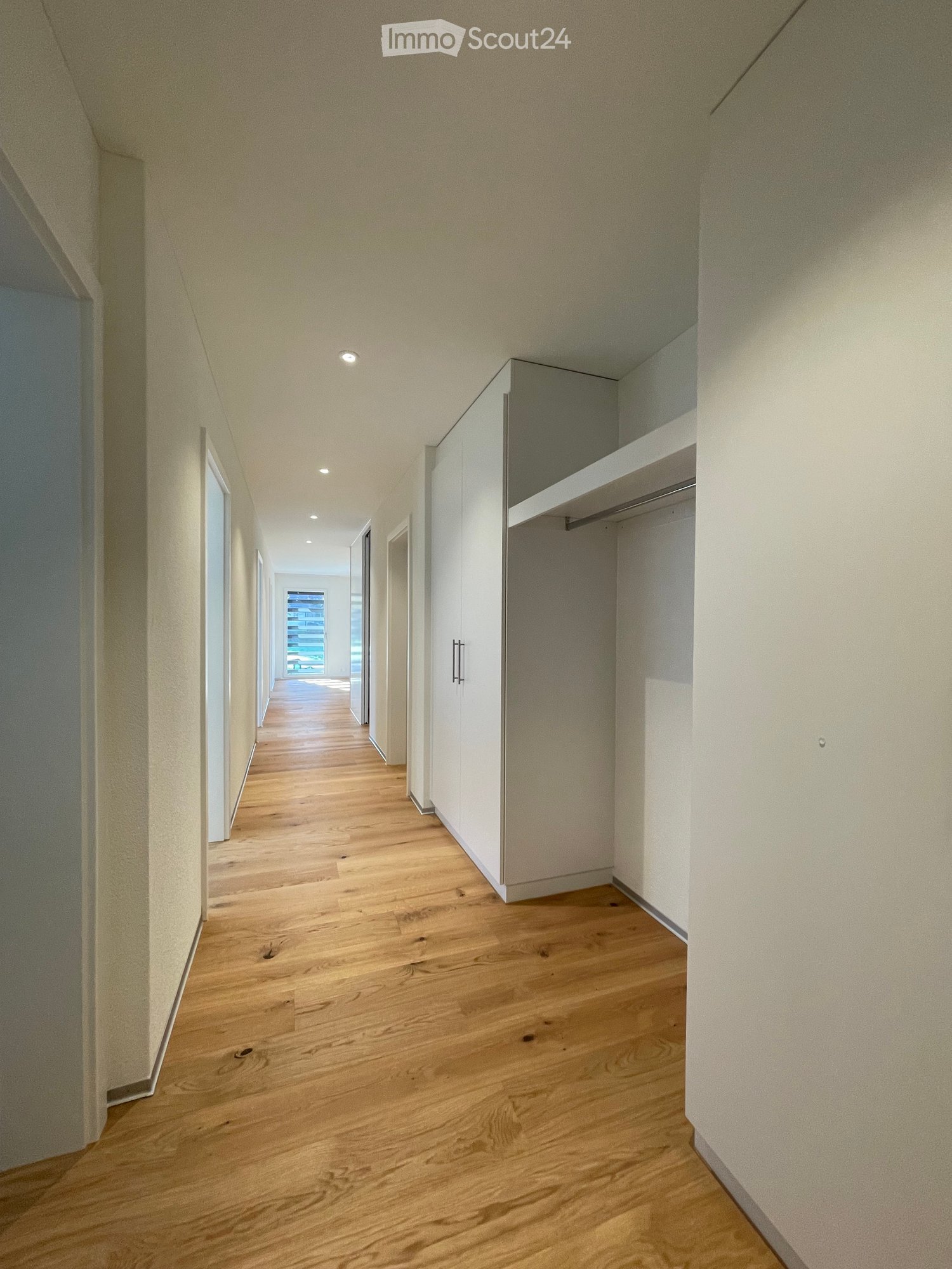 long hallway with white walls, wooden floors, built-in wardrobes