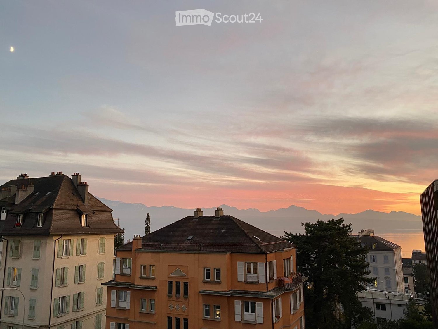 cityscape view of a buildings overlooking mountains and a sunset sky with a moon